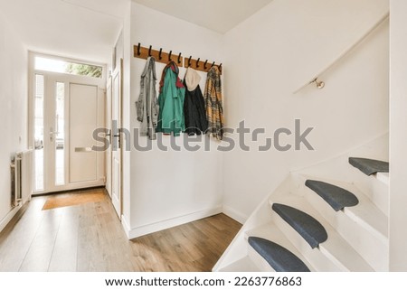 a hallway with white walls and wooden flooring there is a coat rack on the wall next to the stairs