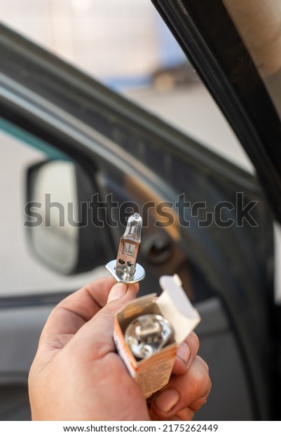 A halogen\
light bulb in a man\'s hand. A professional worker changes the new\
halogen lamps of the car. Car\
repair