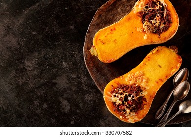 Halved Roasted Butternut Squash With Spicy Filling Viewed Overhead On A Rustic Flat Metal Plate With Spoons And Copyspace For Healthy Seasonal Autumn Cuisine