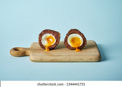  halved scotch egg with runny egg yolk on cutting board