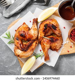 Halves Of Appetizing Grilled Juicy Chicken With Golden Brown Crust Served With Lemon Slices,barbeque  Sauce And Rosemary.