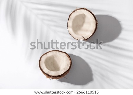 Halves of fresh coconuts and shadow of palm leaf on white background