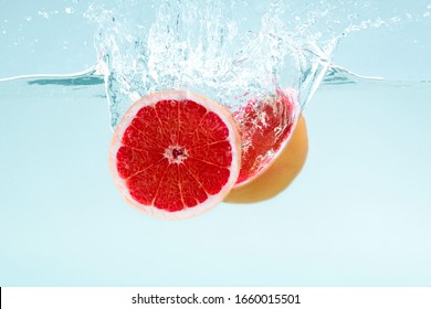 Halves of tasty grapefruit flowing into deep water on blue background