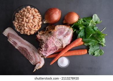 Ham Bone Soup With White Beans And Kale  Ingredients: Overhead View Of Hambone, Bacon, And Vegetables On A Dark Background