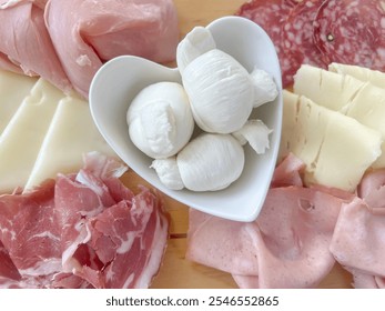 ham and cheese, delicious mozzarella cheese in heart shaped bowl on plate with variety of sliced prosciutto ham an salami as a starter plate in bistro. Italian starter plate with ham and mozzarella. - Powered by Shutterstock