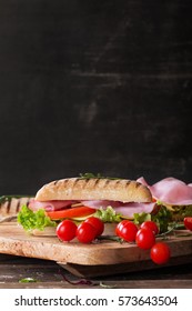 Ham and cheese panini sandwich with salad and cherry tomatoes served on rustic wooden board over an old wooden background with the space on top
