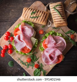 Ham and cheese panini sandwich with salad and cherry tomatoes served on rustic wooden board over an old wooden background. Top view. Square image
