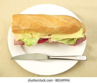 A Ham And Cheese Salad Baguette On A Plate With A Knife From Above