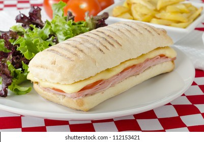 Ham & Cheese Toastie - Cheese, ham and tomato toasted panini served with salad and chips on a red and white gingham background.