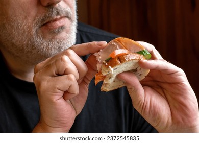 Ham sandwich in hands man. Guy is having lunch with homemade snack. Human eats sandwich with vegetables. Ham and cucumbers on slice bread. Man eats delicious sandwich. Quick snack to satisfy hunger - Powered by Shutterstock