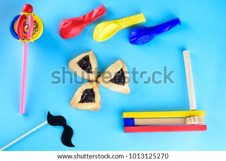 Hamantaschen cookies or hamans ears, wood  colorful noisemakers,funny paper mask mustache on a stick and balloons for Purim celebration (jewish carnival holiday) on blue background.Top view.Flat lay.