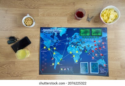 Hamburg, Germany 2.11.21 Board Game Setup For Party With Snacks And Drinks. Pandemic Board Game And Various Food And Drink Appetizers On A Wooden Table