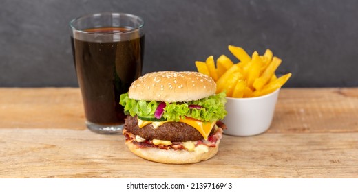 Hamburger Cheeseburger meal fastfood fast food with cola drink and French Fries on a wooden board panorama menu