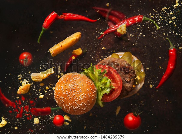 Hamburger divided into parts near to\
vegetables. Levitation food. Advertising still\
life.
