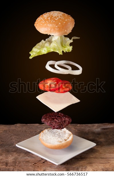 hamburger with flying ingredients placed on\
wooden planks.