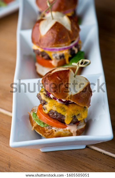 Hamburger mini\
sliders. Traditional classic american restaurant or bar menu item. \
Grass fed angus beef burgers or mini sliders with melted cheddar\
cheese lettuce tomato and onions.\
