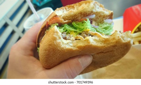 Hamburger With Missing Bite In Hand. Fast Food Unhealthy Eating. 