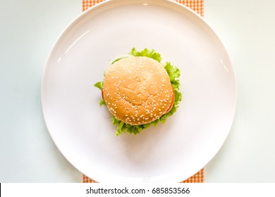 A Hamburger On A White Ceramic Plate And Table Background. Top View.