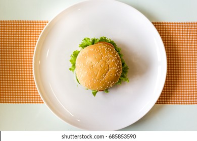 A Hamburger On A White Ceramic Plate And Table Background. Top View.