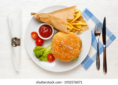 Hamburger, Tomato Sauce, And French Fries In A Paper Bag On A White Plate. Top View