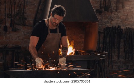 Hammer, anvil and fire with a man working in a forge for metal work manufacturing or production. Industry, welding and trade with a male blacksmith at work in a factory, plant or industrial workshop