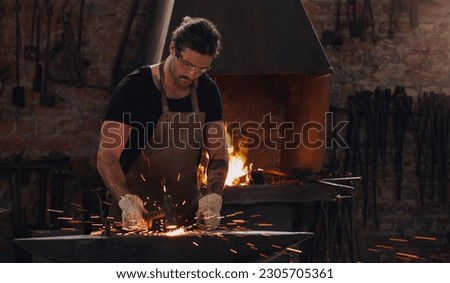 Hammer, anvil and fire with a man working in a forge for metal work manufacturing or production. Industry, welding and trade with a male blacksmith at work in a factory, plant or industrial workshop