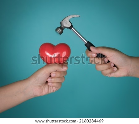 Hammer coming down on red heart against blue background,Failed relationship concept