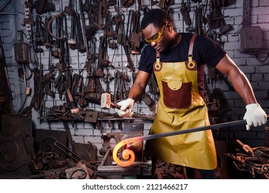 Hammer Industry Small Business Concept.african American Man Dressed In Historical Clothing Is Hammering On The Anvil. A Blacksmith Forges A Metal Product