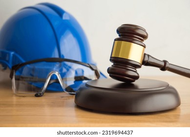 Hammer judge gavel with construction hat helmet, worker safety glasses on wooden background. Labour law concept. Wages, overtime pay, welfare, occupational safety, health, environment, severance pay.
