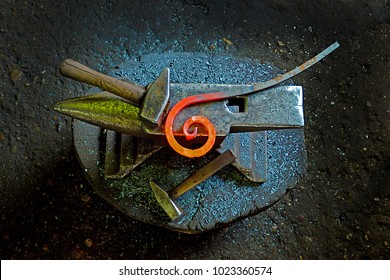 A hammer and a metal object of spiral shape on an anvil. The tool and metal object uses a blacksmith in a blacksmith shop