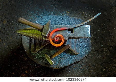 A hammer and a metal object of spiral shape on an anvil. The tool and metal object uses a blacksmith in a blacksmith shop