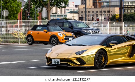 Hammerhead, Yokohama, Japan 7-11-2022: A Custom Metallic Gold Wrapped Lamborghini Aventador At A Mall Parking Lot. Front View Showing Driver’s Side. Other Cars And City In Background In Bokeh.