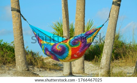 Hammock of rainbow colors hanging between the palm trees on beach. People on summer vacation relaxing in hammock.