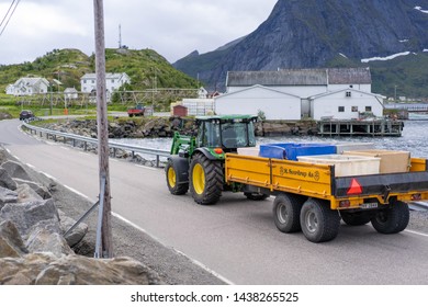 Hamnoy, Norway - June 29, 2018: Tractor Pulling Trailer On Road Toward Reine In Hamnoy On Cloudy Weather, White Building In Background.