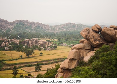 Hampi, India. Boulder Rocks On Hill, Fields In Foreground