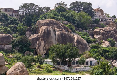 Hampi, Karnataka, India - November 4, 2013: Looking South From Nandi Monolith Statue Temple Ruins. White House Hidden Under Green Vegetation In Front Of Huge Brown-black Rock. Silver Sky.