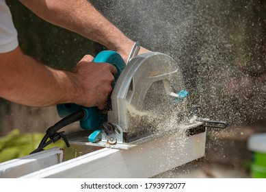 Hampshire, England, UK. 2020. Carpenter holding a circular saw to cut a plank of wood which creates a fine wood dust.