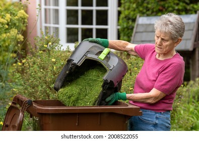 Hampshire, England, UK. 2021. Woman Emptying Grass Cuttings Into A Garden Waste Brown Wheelie Bin.