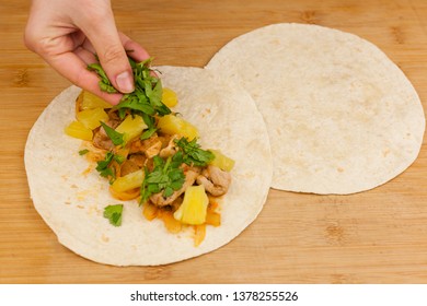 Hand adding chopped parsley to a tortilla for making pork pastor tacos with onion, pineapple and lime on a wooden cutting board background.. Fresh mexican food. 