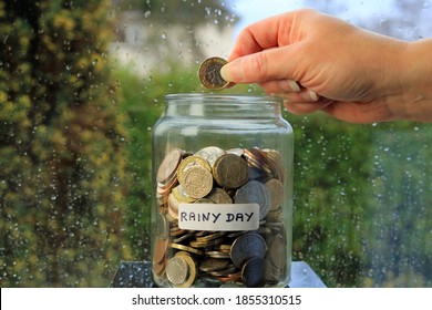 A Hand Adding A Pound Coin To A Glass Jar. Saving Money For A Rainy Day Concept.