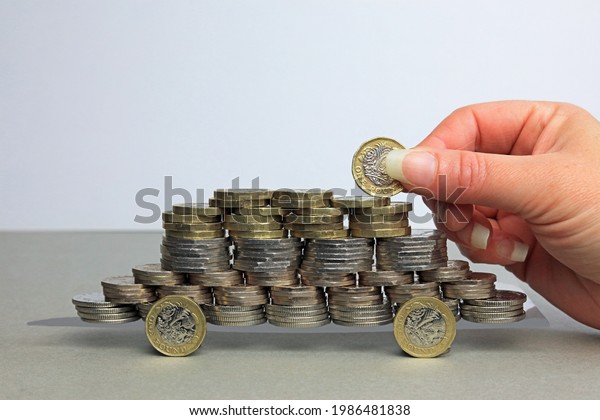 A Hand Adding A Pound Coin To A\
Pile Of Coins. The Rising Costs Of Owning A Car\
Concept.