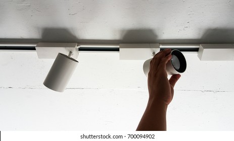 Hand adjust LED downlight lamp on white ceiling.