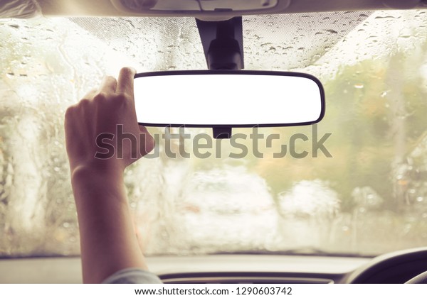 hand adjusting on car rear view mirror with\
raining outside