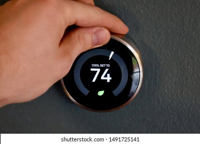 Hand adjusting temperature on smart thermostat to save energy and money. Green tech!