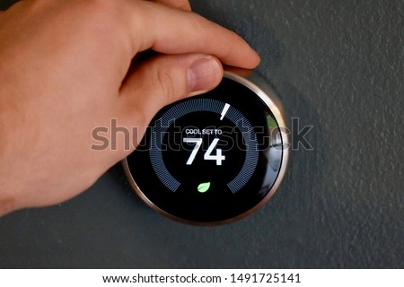 Hand adjusting temperature on smart thermostat to save energy and money. Green tech!