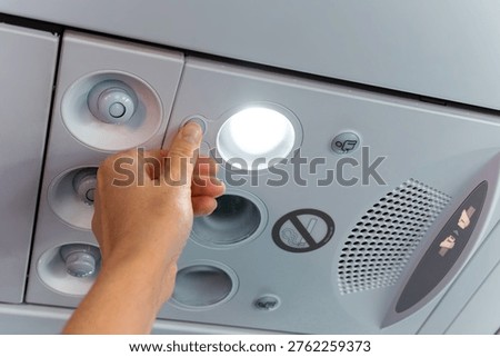 Hand adjusts light switch on airplane overhead panel, showcasing air vent and control buttons for passenger convenience and comfort during flight