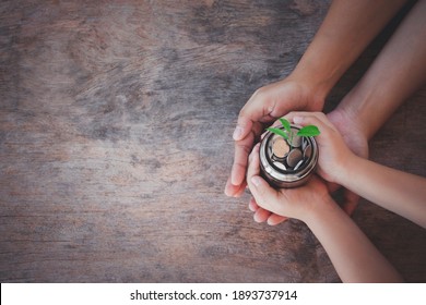 Hand Of Adult And Child Holding A Glass Jar And Plant Is Growing On Top, Family, Home, Education For Their Child, Finacial Concept, Invesment For Starting Up,next Step For Future On Wooden Background.