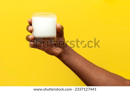 hand of african american man holds glass of milk on yellow isolated background, the hand shows and advertises dairy product, close-up