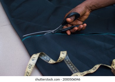 Hand of an African female tailor or fashion designer cutting a measured cloth with scissors to make desired dress in a tailoring workspace