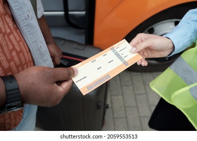 Hand of African passenger with suitcase passing his ticket to young female conductor